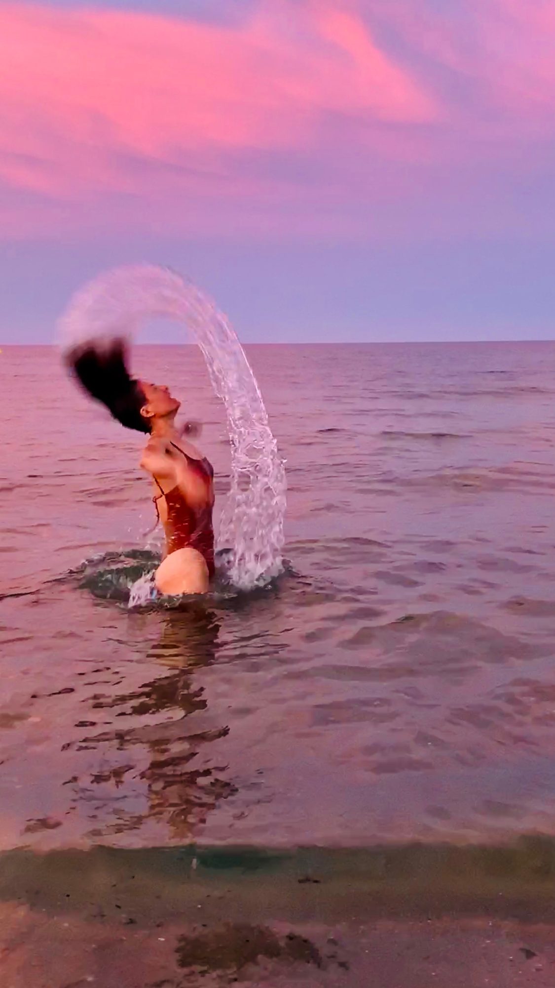 Anna en el mar al atardecer lanzando agua con el pelo